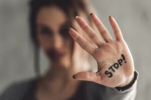 Portrait of young girl with bruises on her face showing stop sign, palm in focus