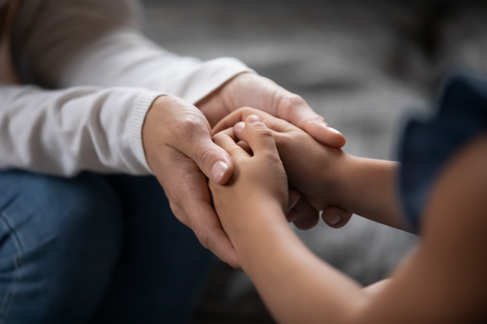 compassionate young foster parent holding hands of little kid girl, giving psychological help, supporting at home